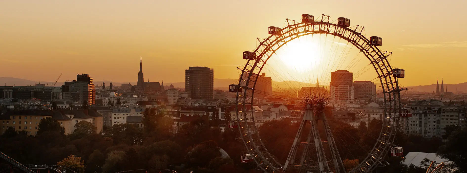 Riesenrad im Wiener Prater, im Hintergrund Wiener Skyline im Sonnenuntergang