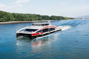 The high-speed catamaran Twin City Liner sails on the Danube with alluvial forest in the background.