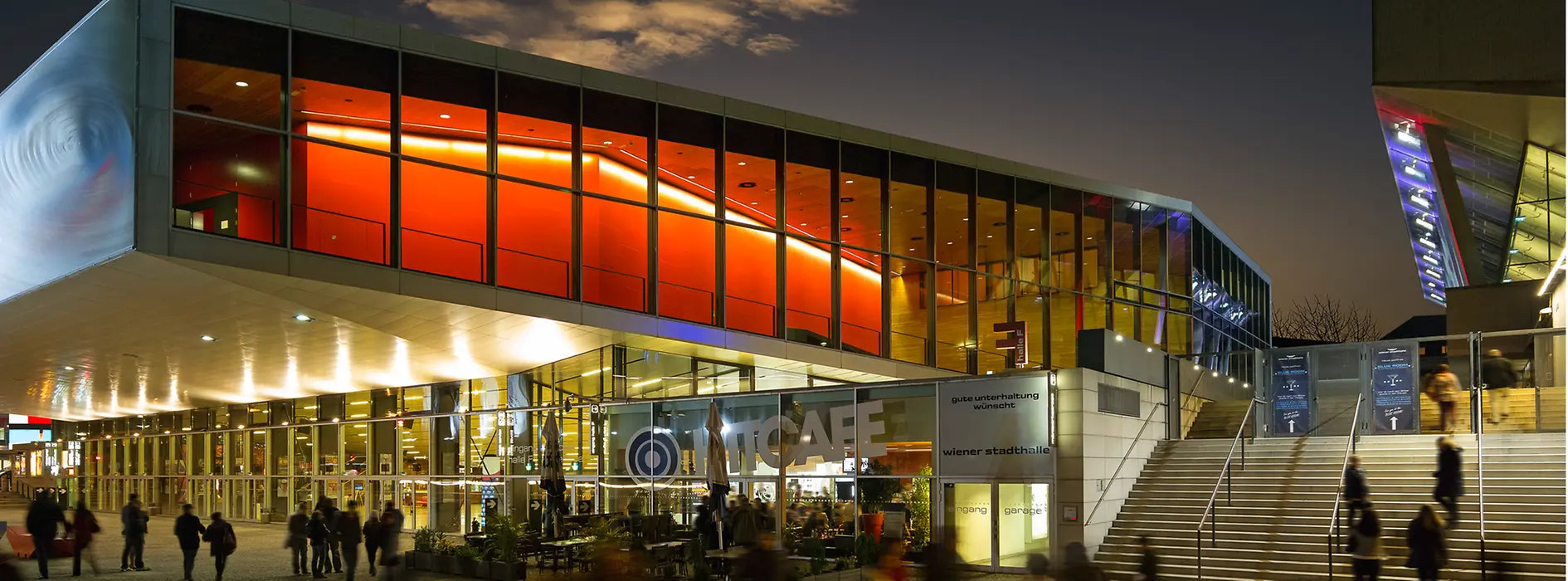 Wiener Stadthalle, abends mit Lichtern in gelb und rot, Besucher