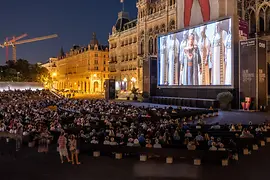 Film Festival on Rathausplatz, many people watch a movie on a screen.