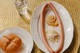 Two plates, on one a couple of Sacher sausages, on the other a bread roll