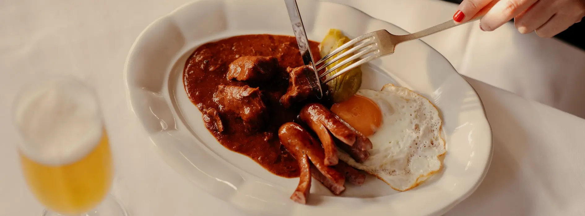 A plate of Fiakergulasch (goulasch) with boiled potatoes, fried egg, and a sausage