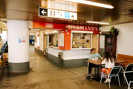 A sausage stand, in front of it a couple sitting at a table