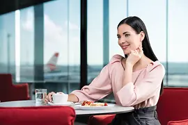 Une femme brune attend son vol dans le lounge Austrian Business avec une tasse de Melange et une part de gâteau.
