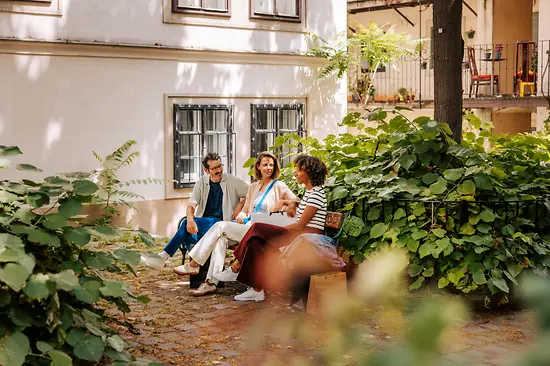 Zwei Frauen und ein Mann auf einer Bank in einem begrünten Innenhof