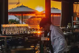 Hote Motto Rooftop-Bar Chez Bernard, barman mélangeant les boissons, coucher de soleil en arrière-plan