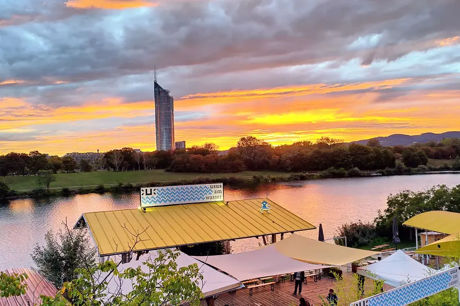 Schanigarten, Usus am Wasser, Wiener Skyline mit Sonnenuntergang im Hintergrund