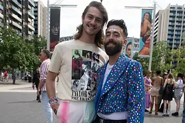 Two men in front of a Taylor Swift concert wearing glitter jackets