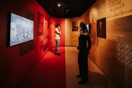 Zwei Besucher in einem in gelb und rot gestalteten Ausstellungsraum vor Screens.