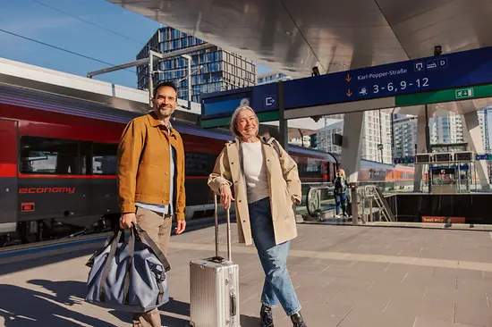 A couple is standing in front of a train on a platform at Vienna Main Station. 